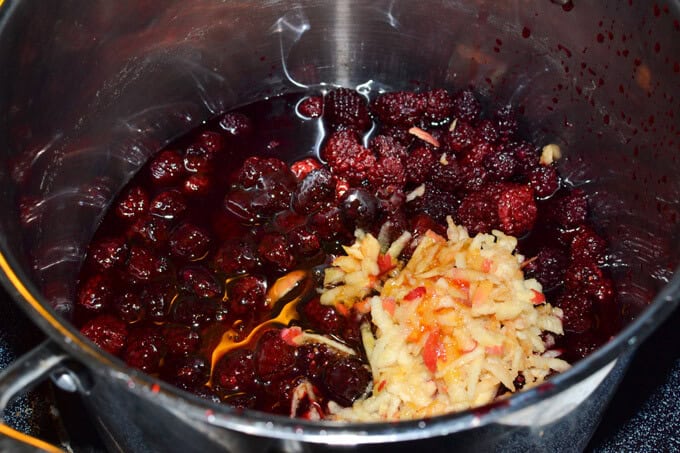 grated apples and blackberries with honey added in a stockpot to make black berry jam
