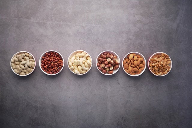 Small white bowls next to each other containing various nuts on concrete.
