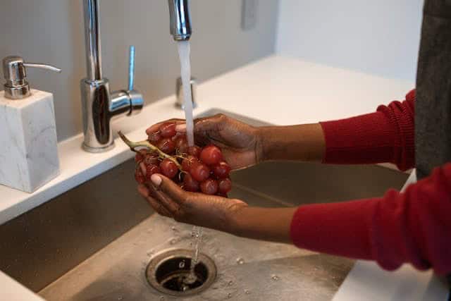 a woman standing next to sink washing grapes