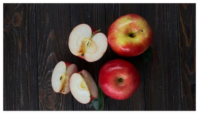 Above view of some whole and cut up red apples on a wooden surface.