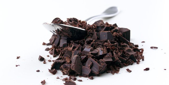 Chopped chocolate on a white surface with a spoon resting on it.