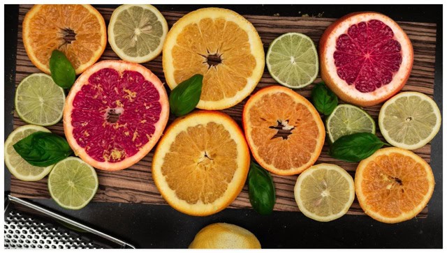 A variety of sliced citrus fruits lying flat on a wooden cutting board.