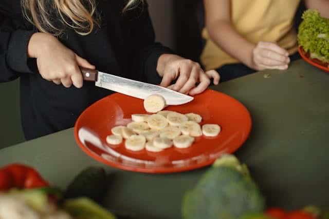 A woman slicing a banana onto a red plate.