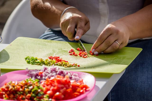 A woman slicing vegetables on a green cutting board.