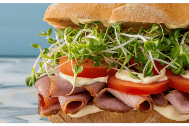 Alfalfa on a sandwich with tomatoes, mayonnaise, and deli meat.