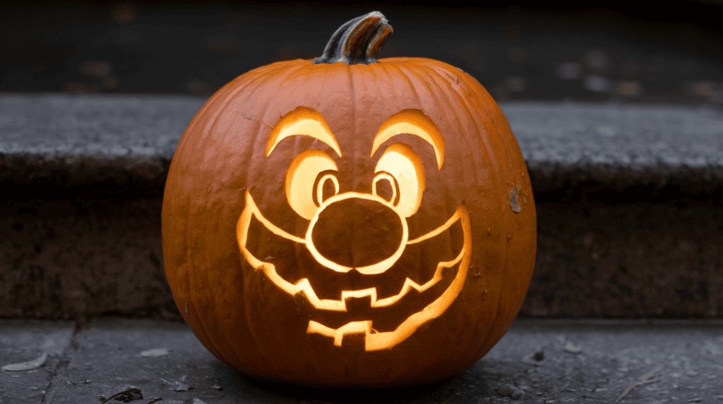 A jack-o-lantern with Mario's face carved into it. The pumpkin is placed on a step. The background is dark.
