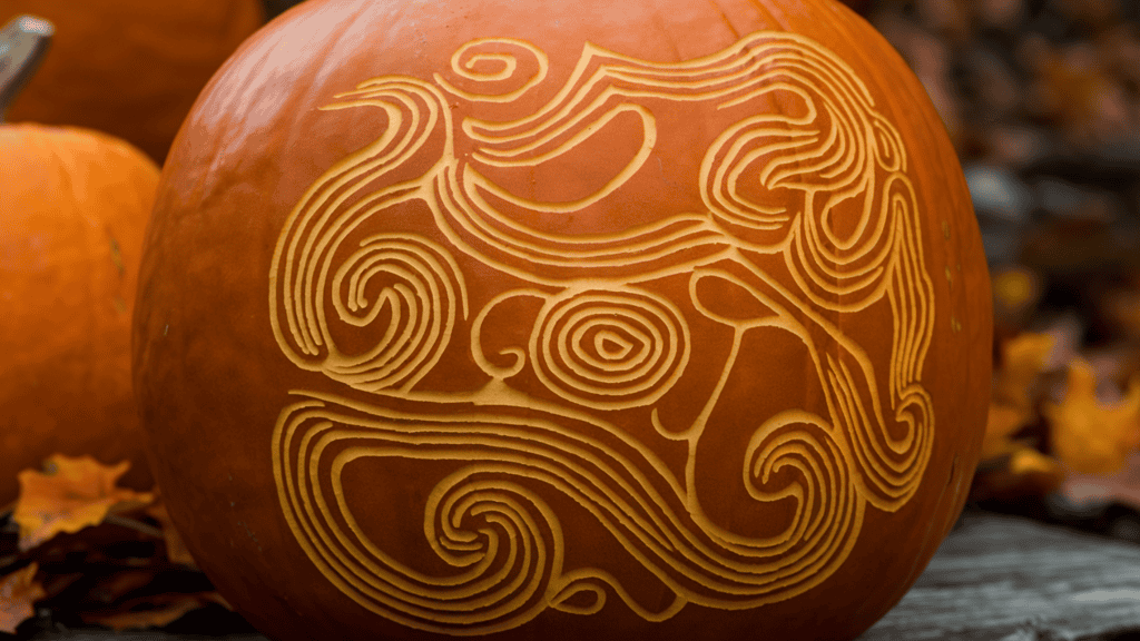 A carved pumpkin with a flowing abstract design. The design features varying line weights and includes swirls, loops, and organic shapes. The pumpkin is placed on a wooden surface. The background contains other pumpkins and autumn leaves.