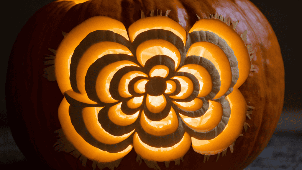 A glowing pumpkin with an intricately layered carving design. The design has distinct depth levels. The pumpkin has a warm orange hue from a light source inside the pumpkin. The background is dark.