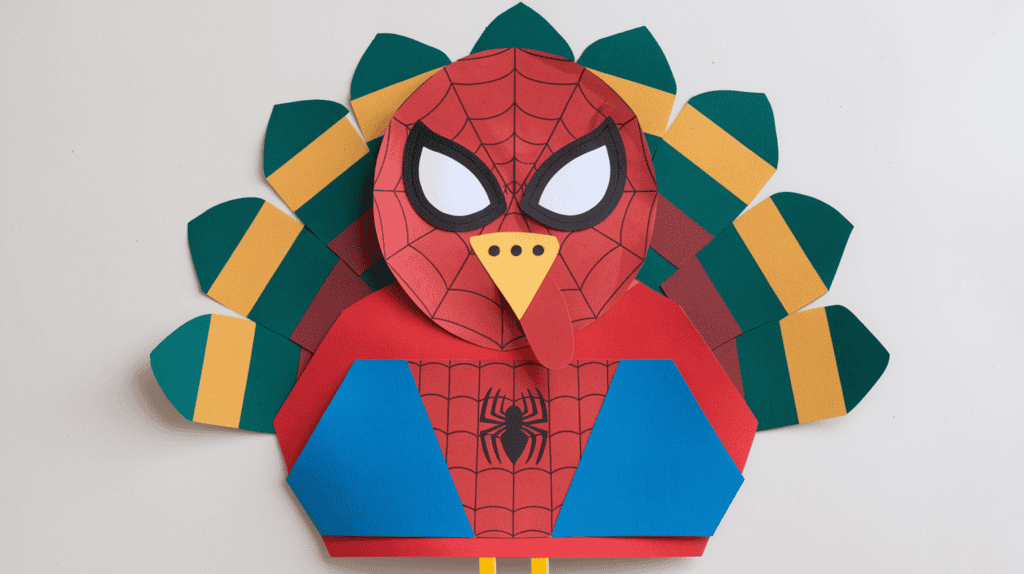 A Spider-Man turkey disguise idea. The craft has a red and blue body with a white head and beak. The turkey is wearing a Spider-Man mask. The craft is placed on a white background.