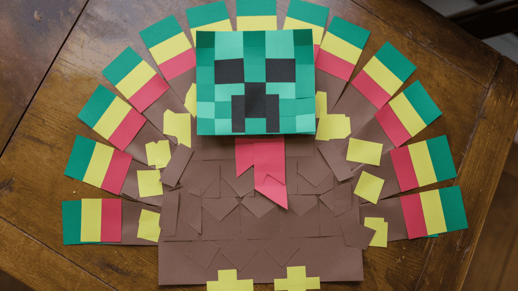 A Minecraft Creeper Turkey disguise idea made of construction paper. The craft has a Creeper face and is shaped like a turkey. The background is a wooden table.