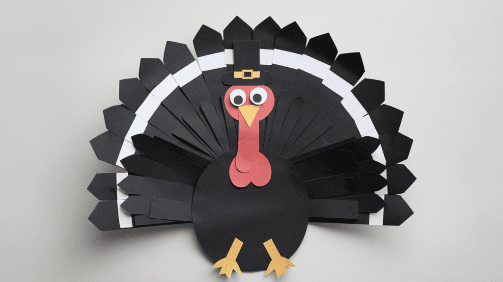 A photo of a turkey disguise idea made with black paper. The turkey has its wings outstretched and is wearing a tiny top hat. The turkey is placed on a white background.